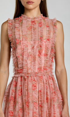 Wearing the Long Formal Dress: Mac Duggal 8309, a woman stands against a neutral background. This sleeveless pink floral midi dress features elegant vertical ruffle details.