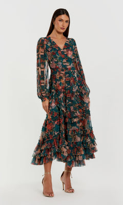A woman stands against a white background wearing the Mac Duggal 8348 Floral Wedding Guest Dress, featuring long sleeves, a V-neck, ruffled tiered A-line skirt, and gold high-heeled sandals.
