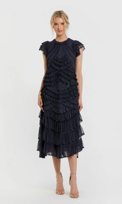 A woman wearing the Mac Duggal 8371 navy midi party dress, featuring a high neckline, micro-ruffle detailing, and flutter sleeves, paired with strappy nude heels and standing against a plain white background.