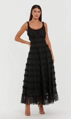 Model wearing the Mac Duggal 8372 Floral Lace Long Formal Dress—a sleeveless, black A-line gown with tiered lace and sheer hem, scoop neckline—posed in front of a plain white background.