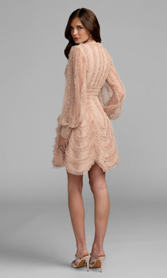 A woman stands facing away against a plain gray background, wearing the Mac Duggal 8392 short party dress—a light pink textured mini dress with bishop sleeves, ruffle details, and a subtle V-neckline.