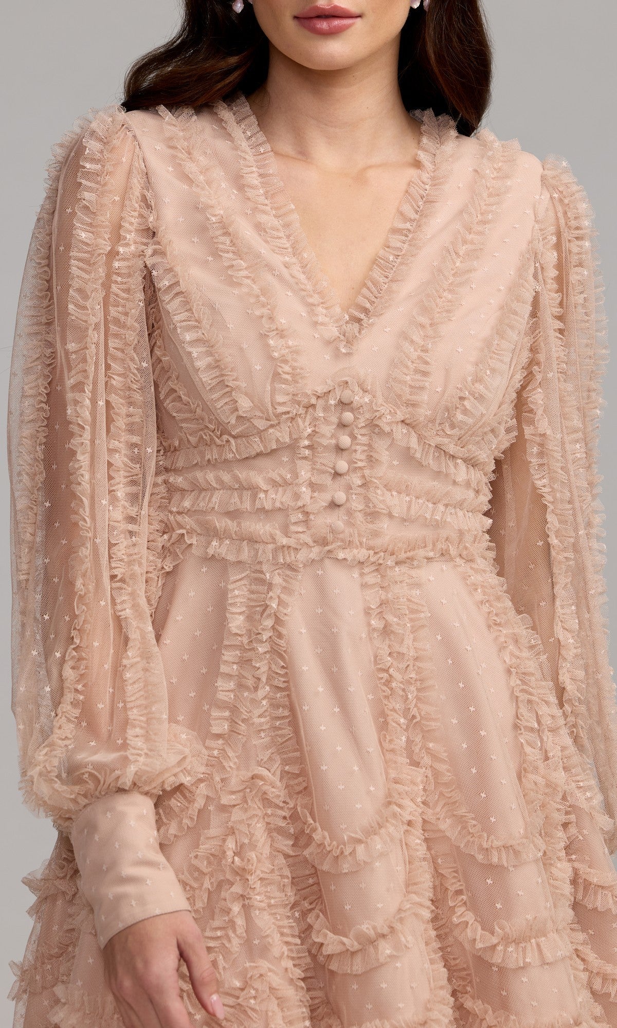 A woman wearing the Mac Duggal 8392 short party dress, featuring light pink textured fabric, ruffles, bishop sleeves, covered buttons on the bodice, and a V-neckline.