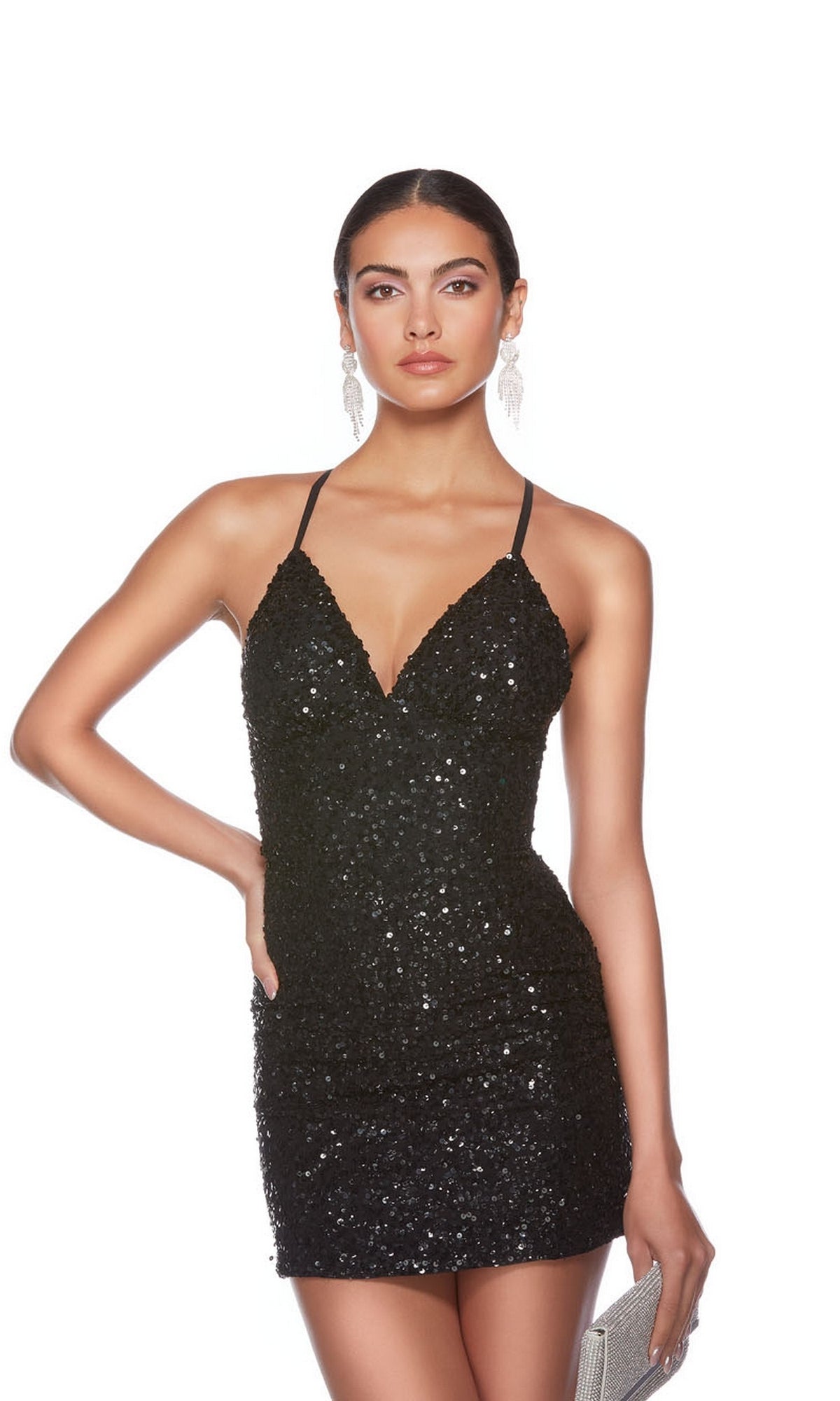 A woman wears the Alyce Empire-Waist Short Sequin Hoco Dress 84000—black, with thin straps—paired with a silver clutch and statement earrings against a white background. This mini dress shines for homecoming or any special night out.