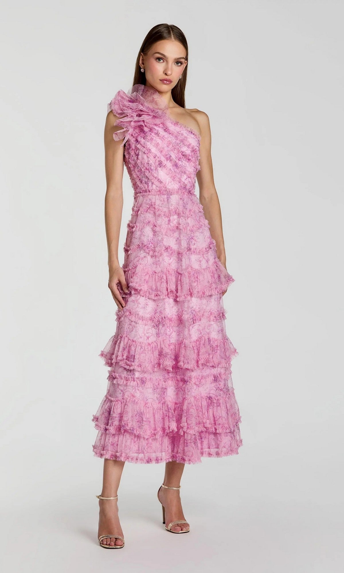 A woman wearing the Mac Duggal 8422 Tea-Length Party Dress in Pastel Multi, featuring a one-shoulder design with tiered ruffle details and matching floral texture, stands against a plain light background.