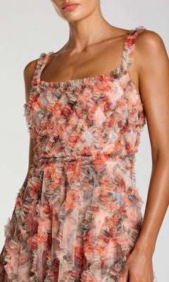 A woman wearing the Mac Duggal 8424 long formal dress, featuring a sleeveless design with a fitted bodice and semi-sheer textured fabric in pink, coral, and gray hues, accented by multi-colored ruffle layers.