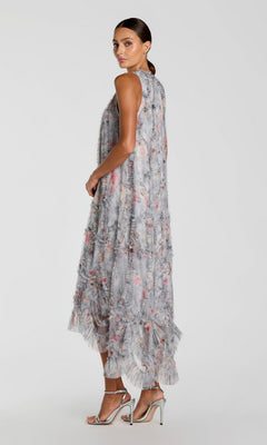 A woman in profile models the Mac Duggal 8430 Midi Party Dress—an ankle-length, ruffled floral cocktail dress with sheer layers—paired with silver high-heeled sandals, posed against a plain light background.