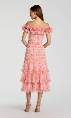 A woman stands facing away, wearing the Mac Duggal 8432 Midi Party Dress—a pink floral design featuring an off-the-shoulder neckline and a ruffle-tiered skirt—paired with nude high-heeled sandals against a neutral background.