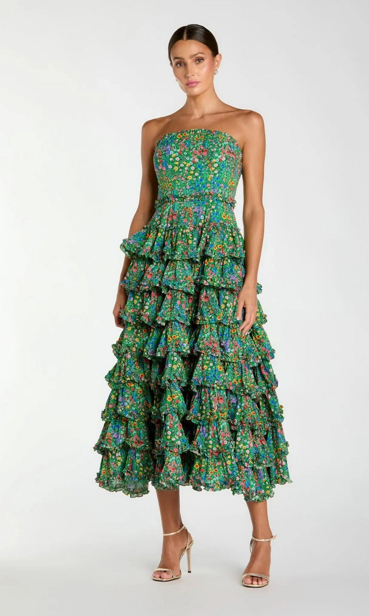 A woman wearing the Mac Duggal 8459 Tea-Length Party Dress—a strapless, green floral-printed gown with multiple ruffled tiers—stands in beige strappy heels against a plain light background.