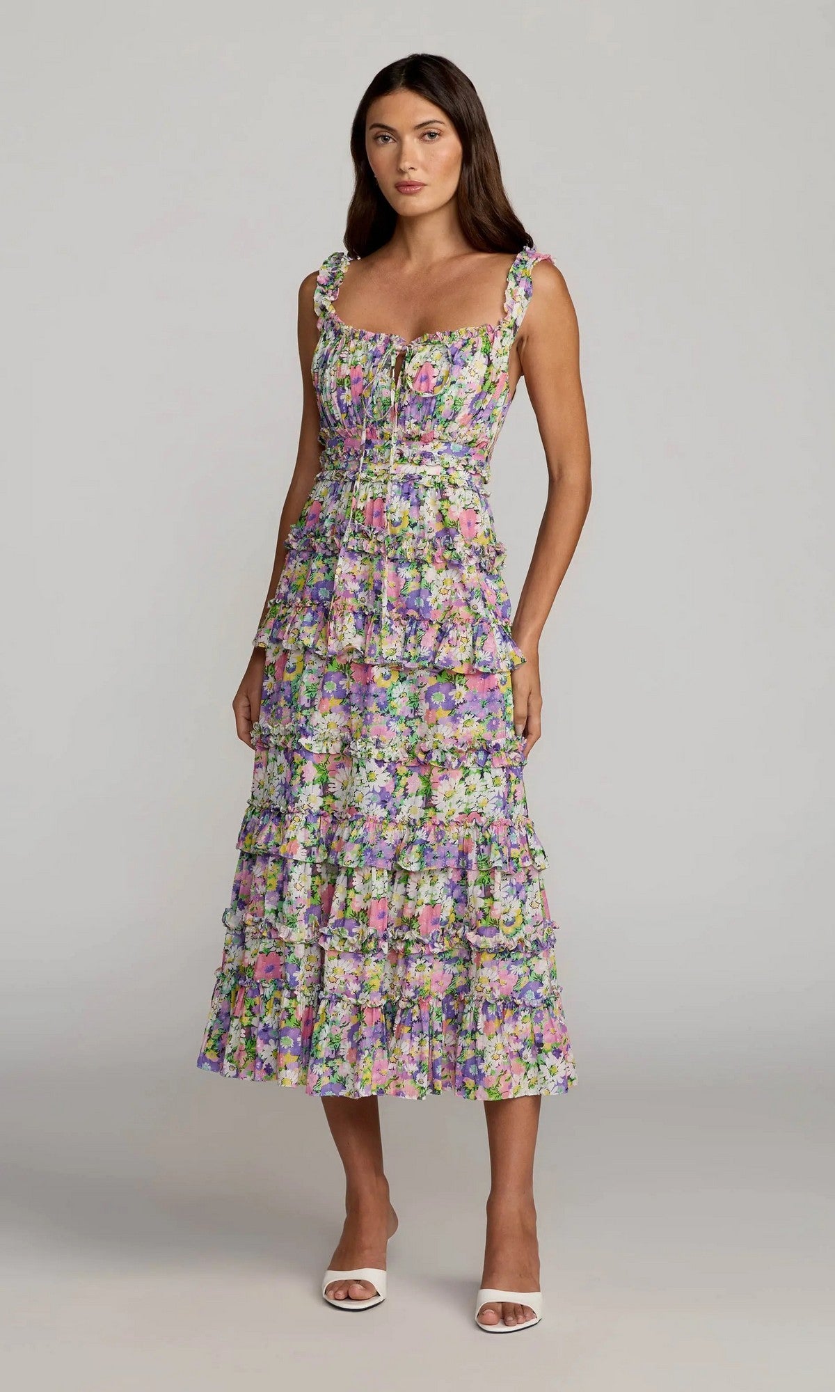 A woman wearing the Mac Duggal 8460 Midi Party Dress in Multi—a sleeveless, floral design featuring ruffle detailing and a tie at the chest—stands in white heeled sandals against a plain background.