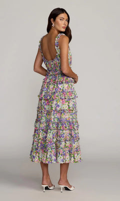 A woman wearing the Mac Duggal 8460 sleeveless, ruffled floral midi party dress and white heeled sandals, standing sideways and looking over her shoulder.