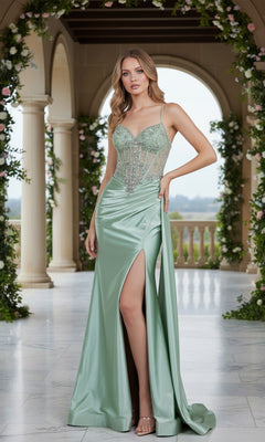 A woman stands on a marble floor in an elegant, columned venue adorned with greenery, wearing the Cinderella Couture 8483J Long Prom Dress in sage, featuring a sheer corset bodice and thigh-high slit with beaded embroidery.