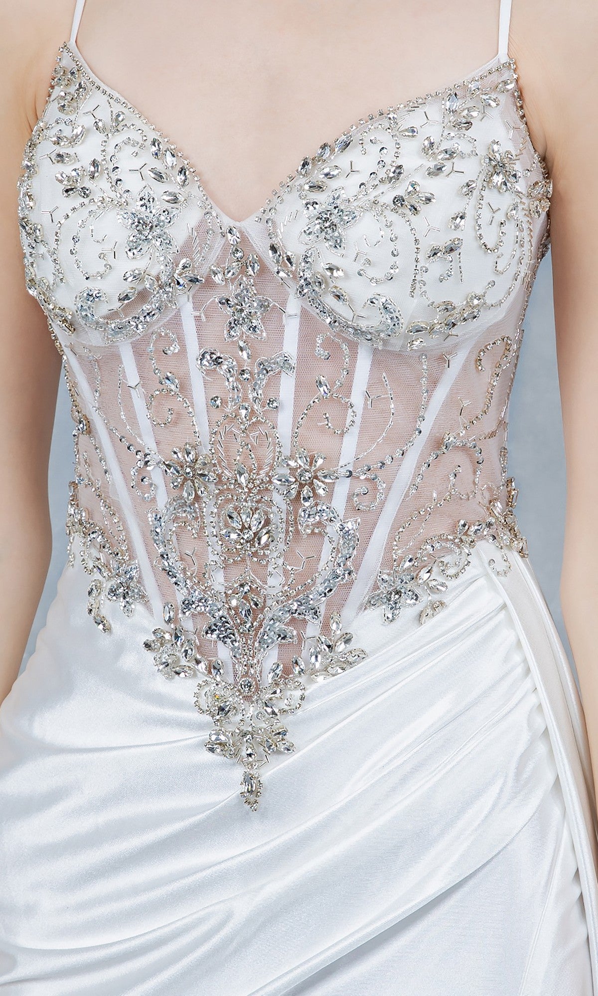 A close-up of the Long Prom Dress: Cinderella Couture 8483J, showcasing its white satin fabric, sheer corset bodice with intricate beaded embroidery, delicate silver details, and thin straps.