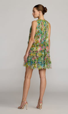 A woman stands in profile against a plain background, wearing the Mac Duggal 8488 Short Party Dress—a sleeveless, knee-length dress featuring multicolored floral patterns and ruffled layers—paired with high-heeled sandals.
