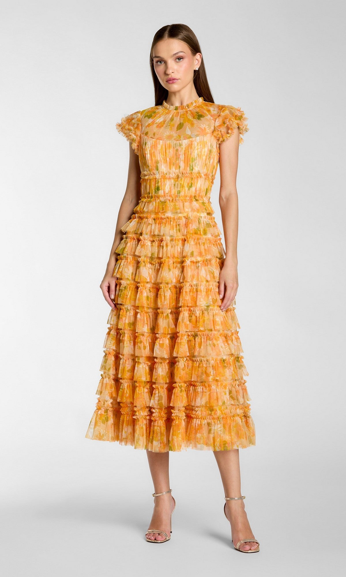 A woman stands in a studio wearing the Mac Duggal 8497 tea-length party dress in yellow multi, featuring ruffles, short sleeves, and paired with strappy high-heeled sandals.