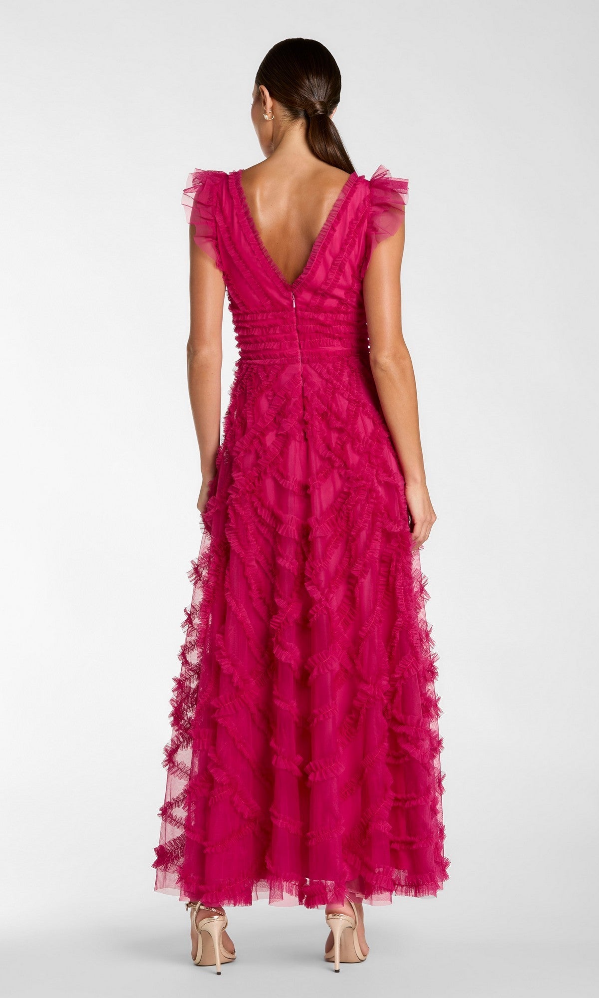 A woman stands with her back to the camera in high heels, wearing the Mac Duggal 8498 long formal dress in fuchsia, which features an A-line silhouette, ruffled floor-length skirt, deep V-back, and cap sleeves.