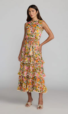 A woman stands against a plain background wearing the Mac Duggal 8500 tea-length party dress in Multi—a sleeveless, tiered floral design featuring layered ruffles and a belted waist—paired with open-toed sandals.