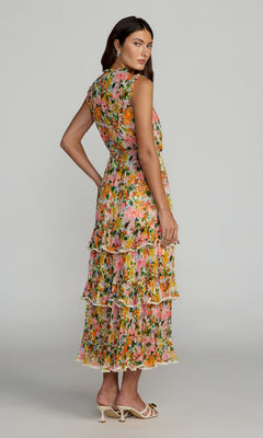 A woman stands in profile, looking over her shoulder, wearing the Tea-Length Party Dress: Mac Duggal 8500—a sleeveless, tiered floral-print dress with ruffles. She pairs the elegant party dress with white heeled shoes, embodying a refined yet playful style characteristic of classic Mac Duggal designs.