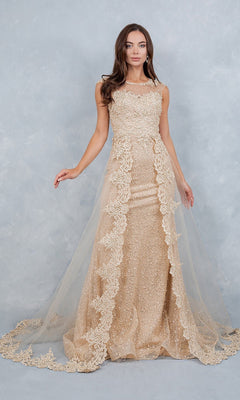 A woman stands posing against a light gray textured background, wearing the Cinderella Couture 8506J long formal dress in champagne—a sleeveless, floor-length gown featuring lace appliques and a sheer tulle fabric overlay.