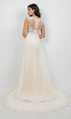 A woman stands facing away, wearing the Long Formal Dress: Cinderella Couture 8506J—a white, floor-length gown crafted from delicate tulle with lace detailing and a sheer back—set against a plain white background.