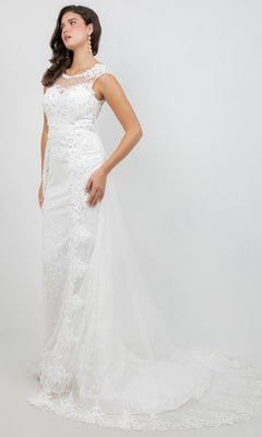 A woman wearing the Cinderella Couture 8506J long formal dress, featuring a sleeveless white lace design with a fitted bodice, illusion neckline, and a sweeping tulle train adorned with intricate lace appliques, stands against a plain light background.
