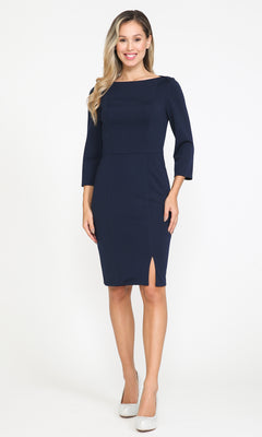 A woman stands against a white background wearing the Classy Knee-Length Career Dress 8526 in navy blue, featuring three-quarter sleeves and a front slit, paired with white shoes.