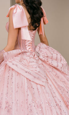 A woman is shown from behind wearing the Quinceanera Dress 8530JQ by Cinderella Couture, a pastel pink ball gown adorned with sequin details and a large bow at the back, featuring a stunning beaded corset bodice.