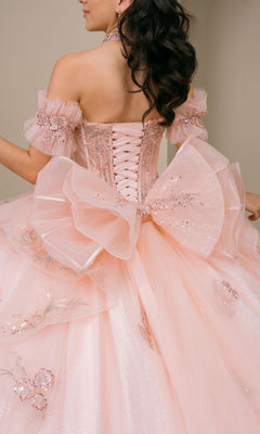 A woman wearing the Quinceanera Dress 8540JQ By Cinderella Couture—a sparkly blush pink gown featuring off-shoulder sleeves, floral details, a corset back, and a large bow—perfect for a quinceanera ball gown look.