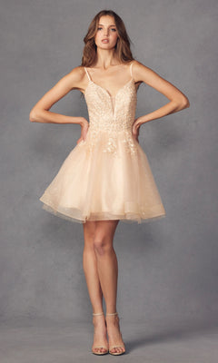 A woman stands with hands on hips, wearing the Short Lace-Up Babydoll Homecoming Dress 859—an a-line light beige short dress with thin straps, floral details, and tulle skirt—paired with strappy heeled sandals against a gray background.