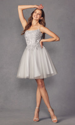 A woman in the Embroidered-Corset Babydoll Homecoming Dress 860—a short, light gray cocktail dress with floral embroidery and a tulle skirt—poses smiling with one arm raised against a plain gray background.