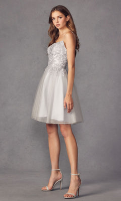 A woman in the Embroidered-Corset Babydoll Homecoming Dress 860, featuring silver floral embroidery and a tulle skirt, stands in profile against a gray background, wearing high-heeled sandals.