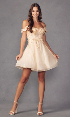 A woman in the Floral Off-the-Shoulder Short Homecoming Dress 861, featuring cream fabric and delicate floral appliqué, stands against a gray background, smiling and posing with hands holding her skirt.
