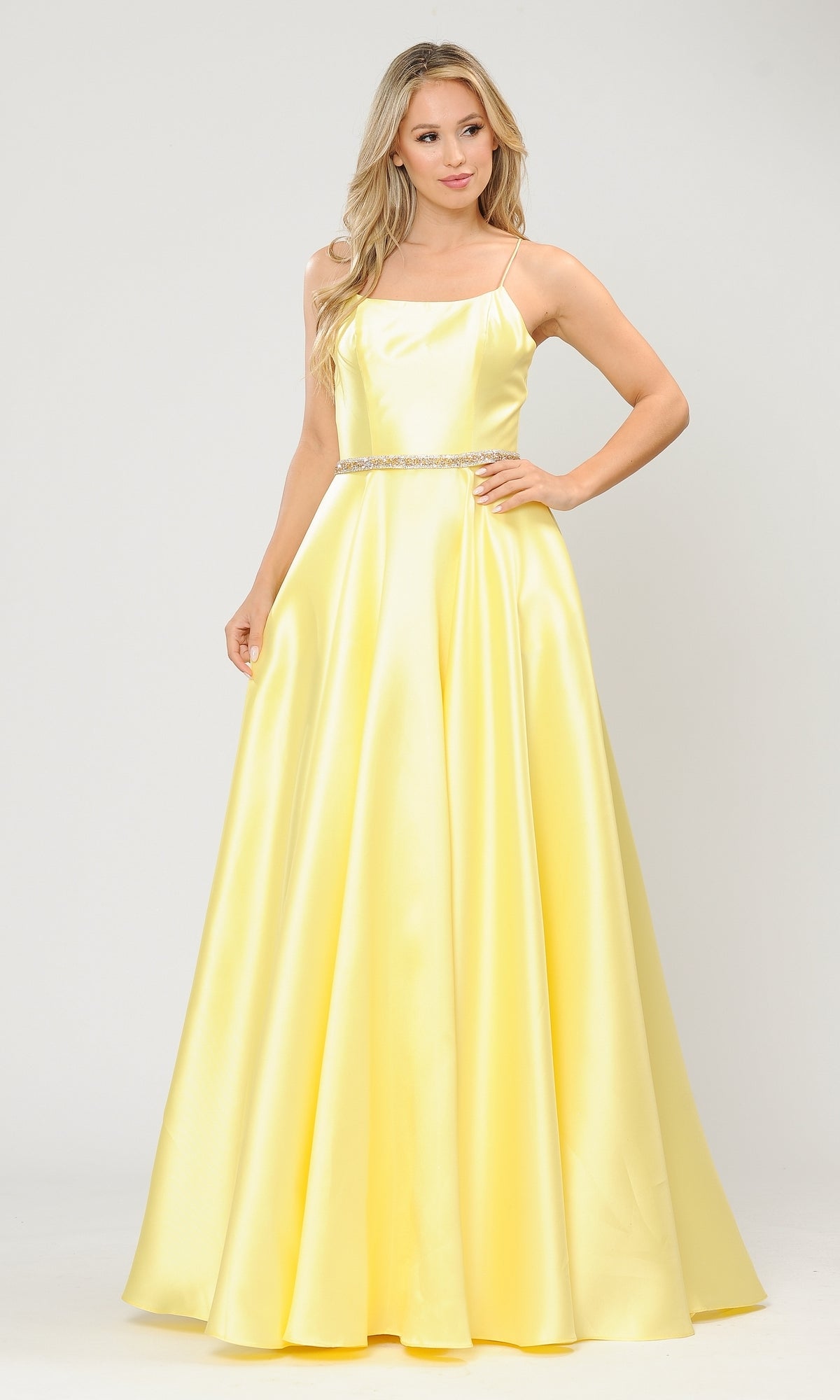 A woman models the Scoop-Neck Long A-Line Prom Dress with Pockets 8684, a sleeveless yellow satin gown featuring a square neckline and thin straps, standing against a plain white background.