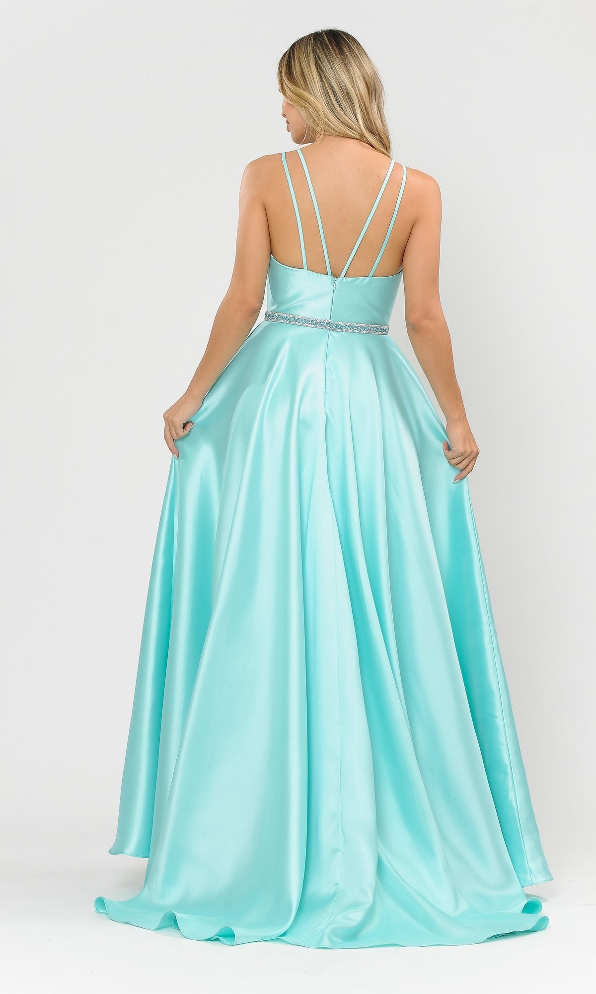 A woman stands facing away, holding the skirt of a light blue Long A-Line Mikado Prom Gown 8690 with pockets and thin crisscross straps, featuring a beaded waistband.