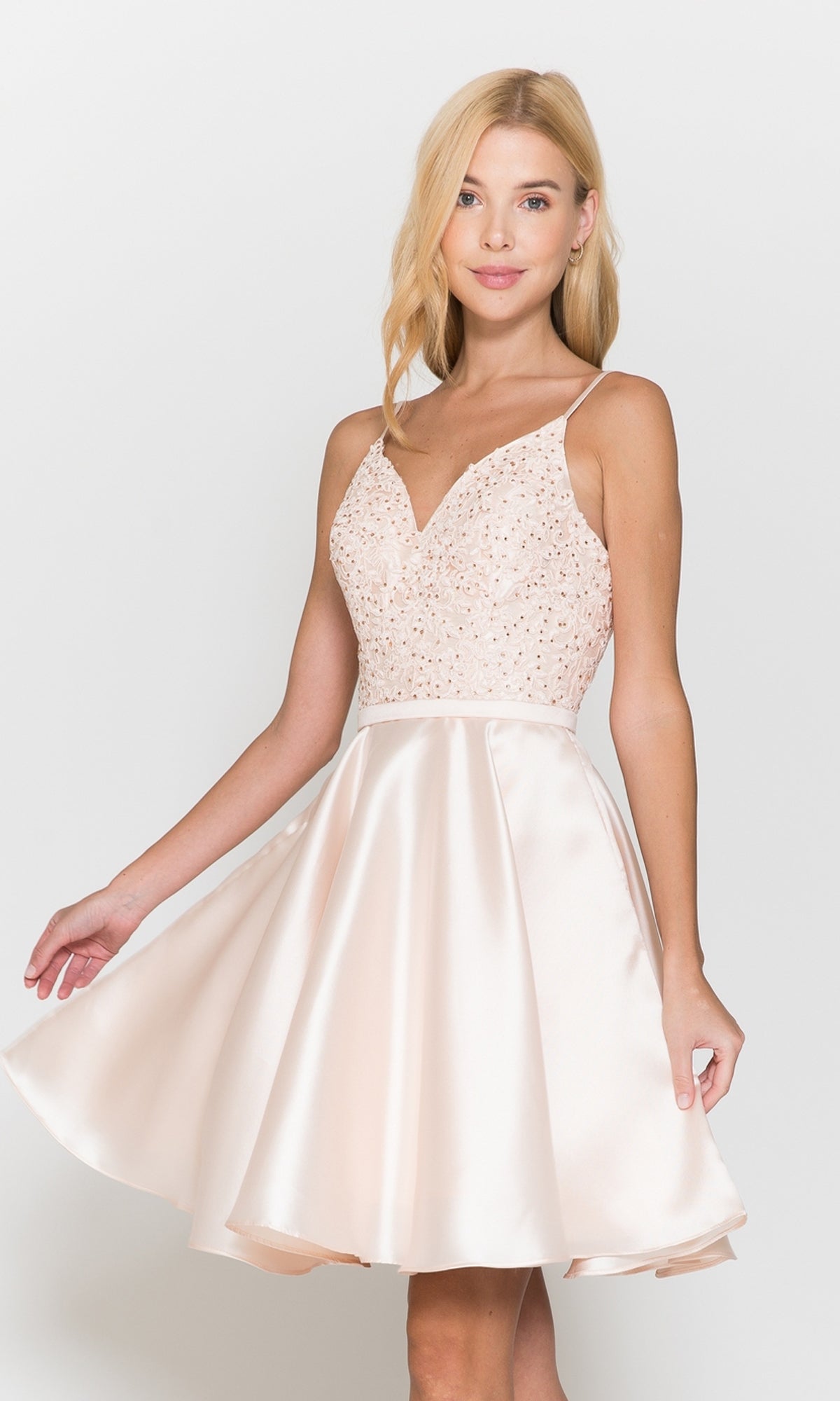 A woman wears the Short A-Line Homecoming Dress with Pockets 8694 in blush, featuring a sleeveless, fitted embellished bodice and flared satin skirt, standing against a plain white background.