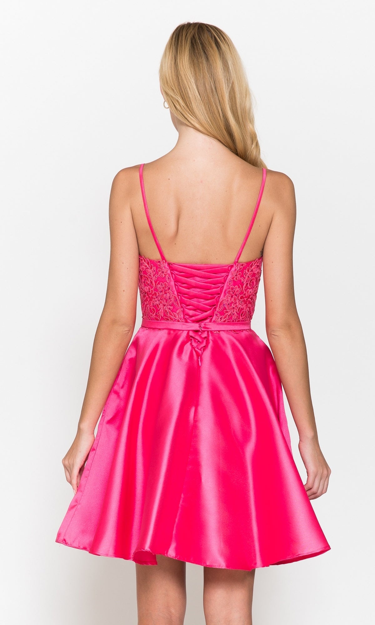 A woman with long blonde hair is shown from the back wearing the Short A-Line Homecoming Dress with Pockets 8694, a bright pink satin dress featuring thin straps, lace bodice detailing, and a flared skirt.