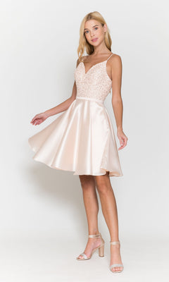 A woman wearing the Short A-Line Homecoming Dress with Pockets 8694, featuring a sleeveless, light pink satin design with a beaded v-neck bodice and flared skirt, stands against a plain white background.