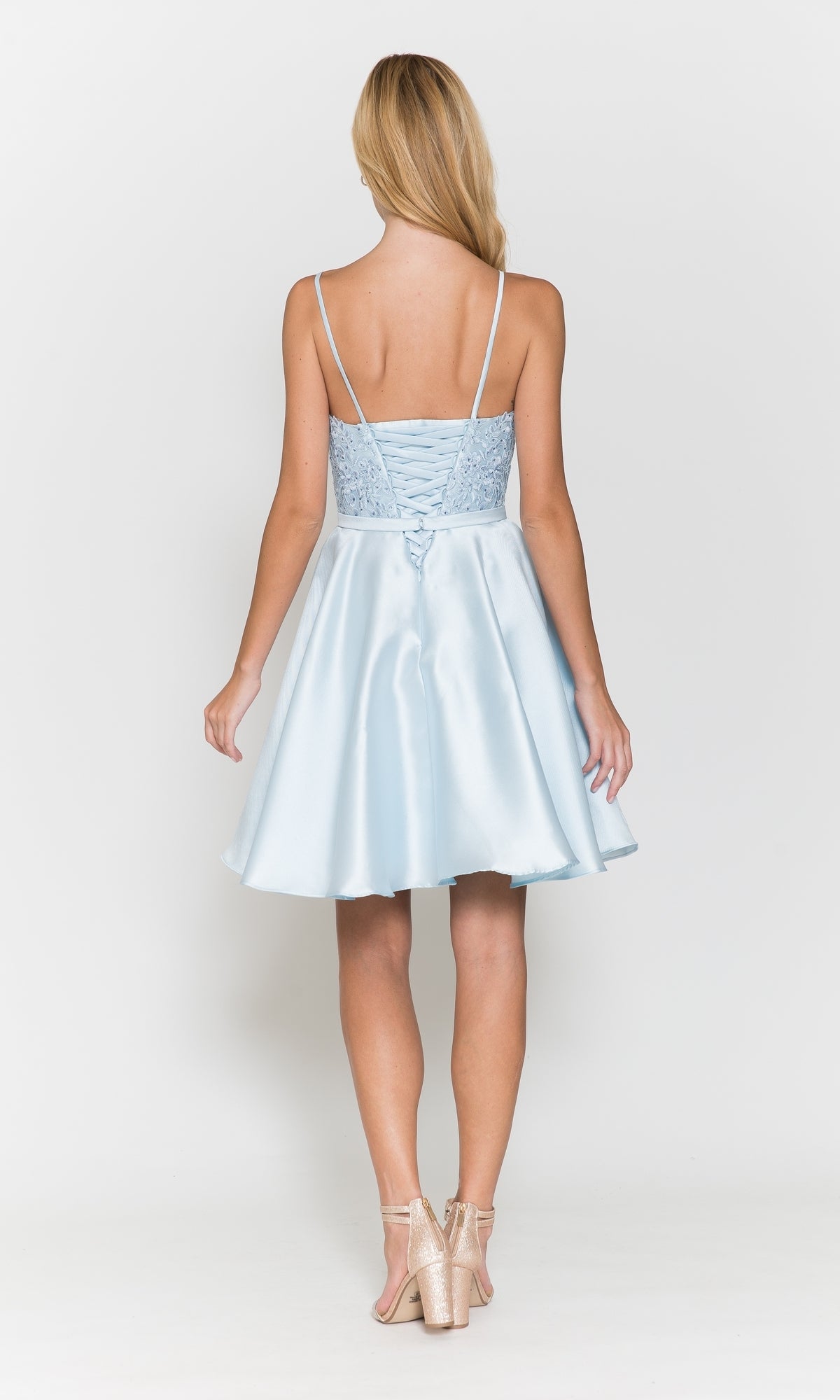A woman with long blonde hair wears the Short A-Line Homecoming Dress with Pockets 8694, a light blue, sleeveless dress with a lace-up corset back and shiny beige heels, shown from behind against a plain white background.