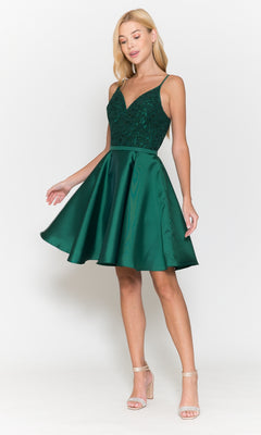 A woman wears the Short A-Line Homecoming Dress with Pockets 8694, featuring a sleeveless dark green lace bodice and flared satin skirt, paired with strappy beige heels, standing against a white background.