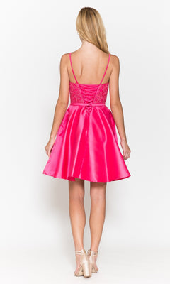 A woman stands facing away in the Short A-Line Homecoming Dress with Pockets 8694, featuring bright pink color, lace details, spaghetti straps, and paired with beige high-heeled shoes.