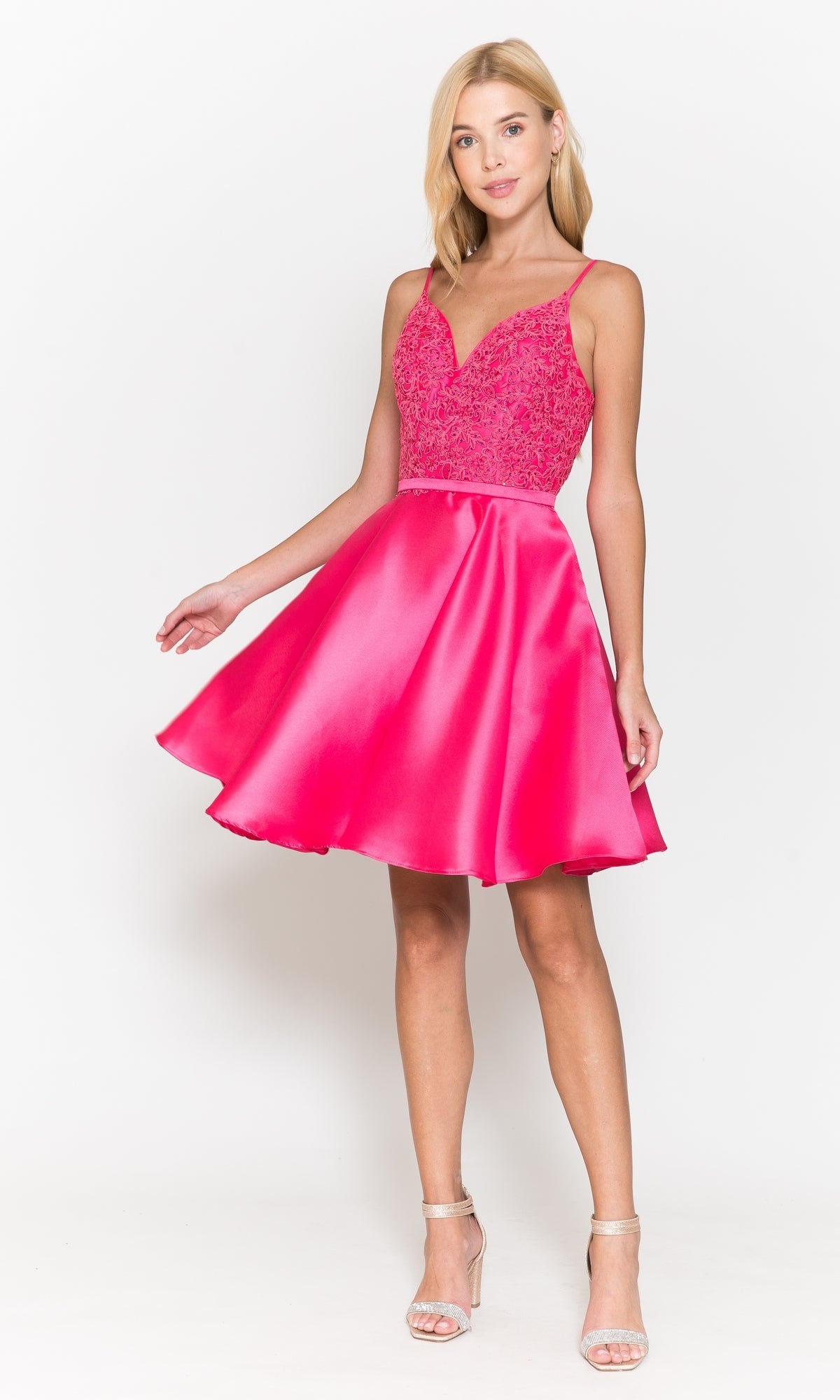 A woman wears the Short A-Line Homecoming Dress with Pockets 8694—sleeveless, bright pink with a lace bodice and flared satin skirt—paired with strappy heels against a plain white background.