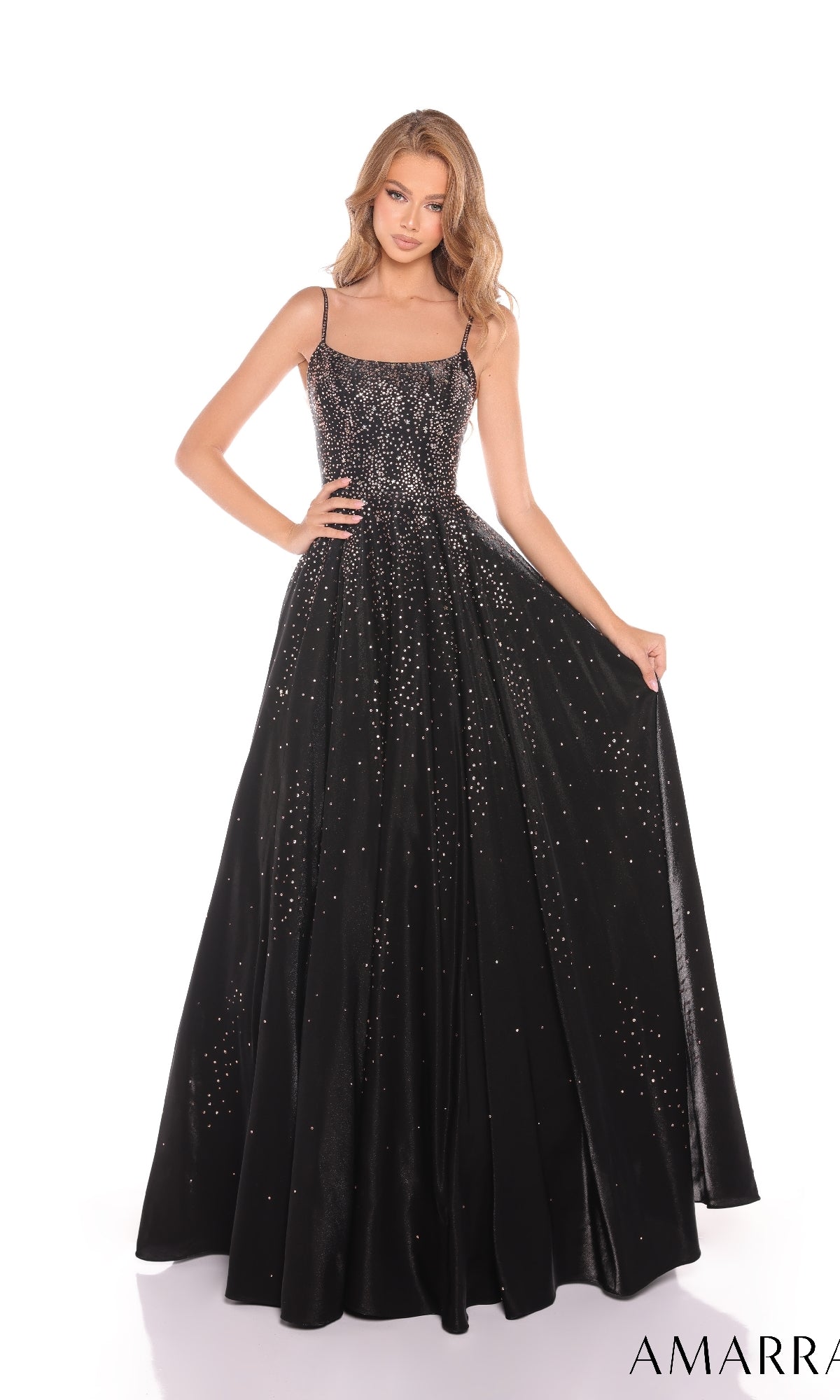 A woman wearing the Amarra 87292 Long Prom Dress?a floor-length black gown with thin straps, sparkling embellishments, and a sleek satin a-line skirt?stands against a white background.