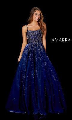 A woman stands smiling against a black background beside the word "AMARRA," wearing the Long Prom Dress: Amarra 87292?a navy blue, floor-length gown with sparkling embellishments and a satin A-line skirt.