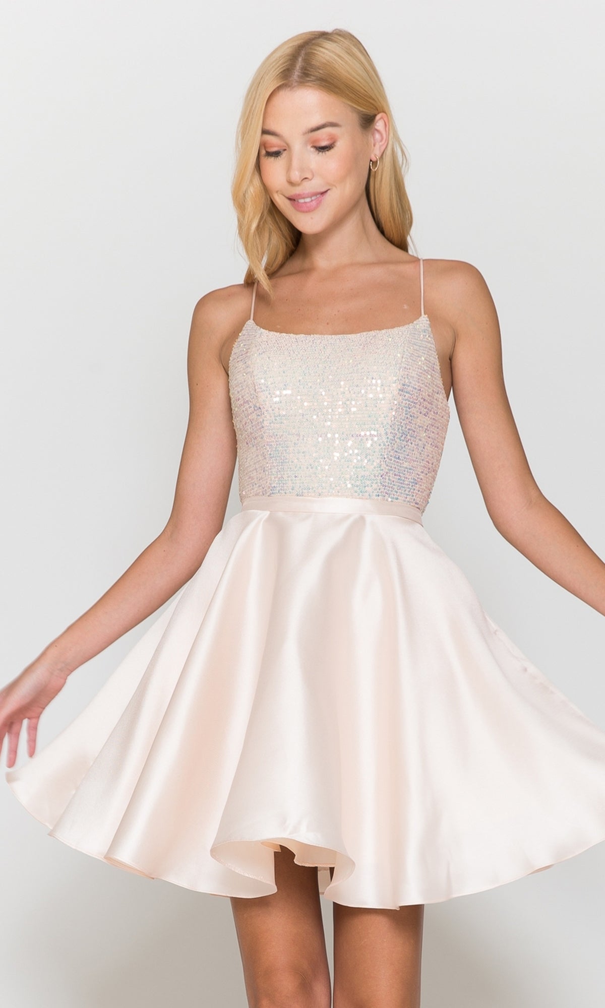 A woman models the Sequin-Bodice Short Flared Homecoming Dress 8730 in blush, featuring a sleeveless sequined bodice and satin skirt, against a plain background.
