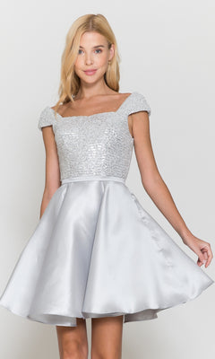 A young woman wears the Cap-Sleeve Short A-Line Homecoming Dress 8732, featuring a silver sequined bodice and satin flared skirt, as she stands against a plain light background.