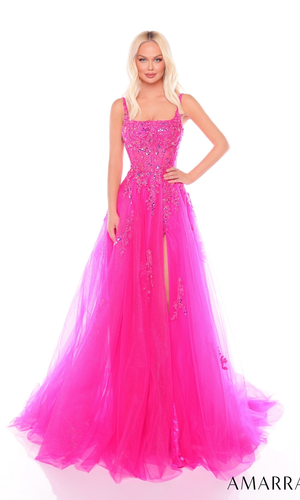 A woman wears the Amarra 88084 Embroidered Prom Ball Gown?bright pink, floor-length tulle with floral embellishments, a corset bodice, and high slit?posing against a plain white background.
