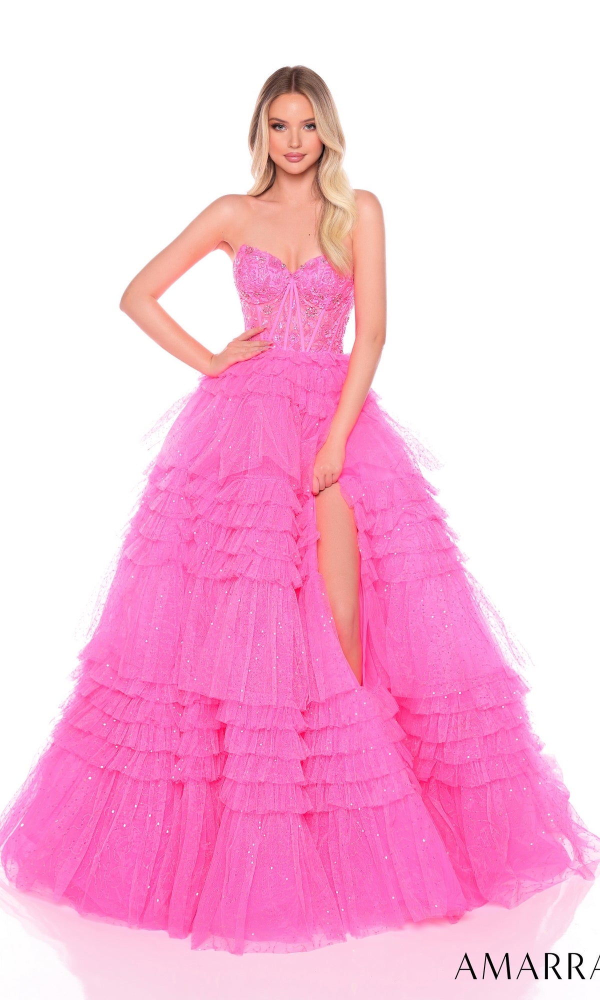 A woman wearing the Long Formal Dress 88099 by Amarra, a bright pink strapless gown with a sheer corset bodice, ruffle layered skirt, and high slit, poses against a white background.