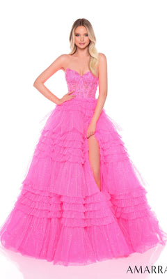 A woman wearing the Long Formal Dress 88099 by Amarra, a bright pink strapless gown with a sheer corset bodice, ruffle layered skirt, and high slit, poses against a white background.