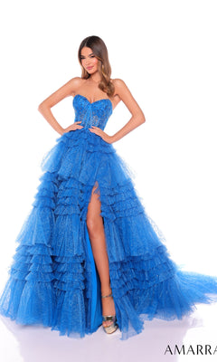A woman poses in the Long Formal Dress 88099 by Amarra, a strapless ball gown with bright blue ruffle layers, a high slit, and a sheer corset bodice, against a plain white background.