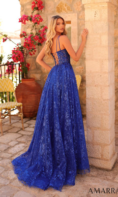 A woman stands outdoors in the Long Formal Dress 88126 by Amarra, a blue lace-embellished A-line gown with a floral pattern and lace-up back, looking over her shoulder amid flowers and stone structures.