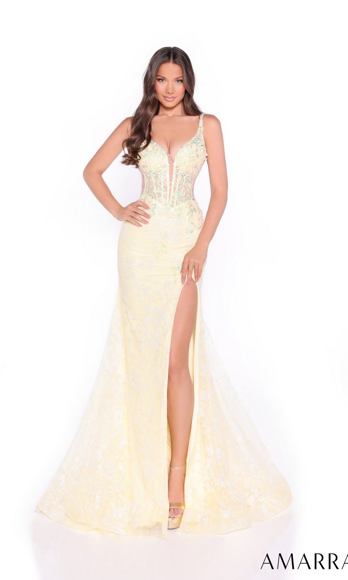 A woman poses against a white background wearing the Amarra 88275 Sheer-Sides Long Glitter Prom Dress, featuring a light yellow color, floor-length mermaid skirt, sheer bodice, floral details, and high leg slit.